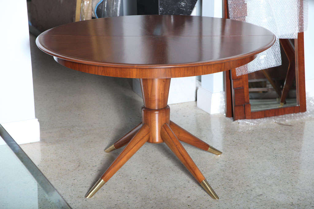 A mahogany dining table on centre pedestal with four tapered legs extending from the centre pedestal ending in brass tips. The table opens with two 18