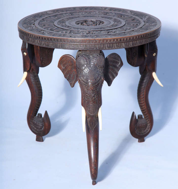 Unusual accent table, having a round top incarved with scrollwork and similarly carved apron; on three legs carved as elephant heads.