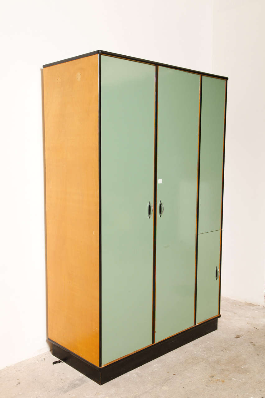 Nice early example of Industrial Design from the Belgium modernist architect. 
Contains inside with two drawers, some shelves and a wardrobe.
Three similar cabinets available. Wooden doors with soft green and black laminated melamine, each one