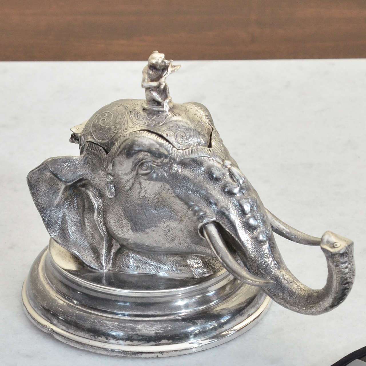 English elephant head inkwell with finial on the lid in the form of monkey playing a flute with glass insert for the ink. The inkwell is on a circular base marked L&W.S for Lee & Wigfull of Sheffield. Similar American silver plate inkwell sold at