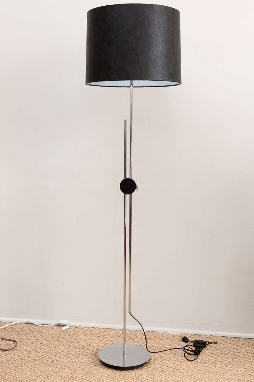 Modernist floor lamp.  Chrome with composite black circle.  Knob turns to adjust height of lamp from minimum 56