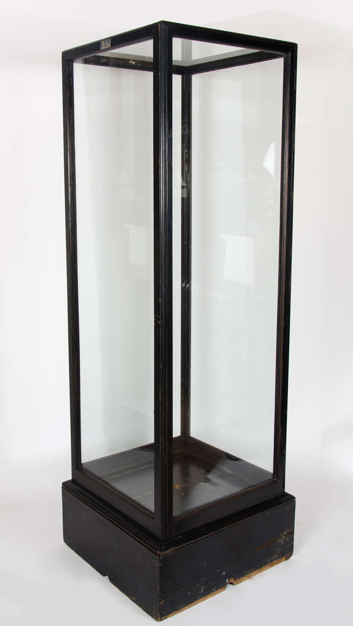 A large antique vitrine or display unit with a solid mahogany frame, painted black. This antique display cabinet has a single door opening.