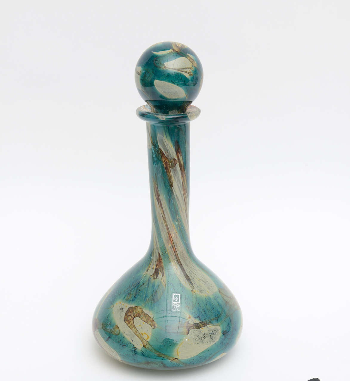 The Malta region of this decanter glass bottle represents the topography of land and sea and earth and forms. It is signed Mdina.