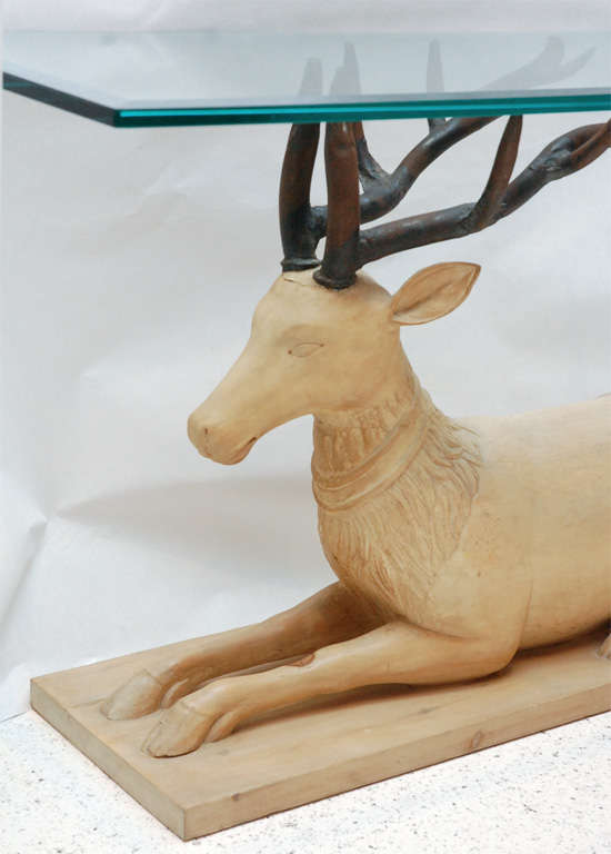 A whimsical console or sofa table with a beveled edge glass top resting on the antlers of a recumbent carved wood stag.