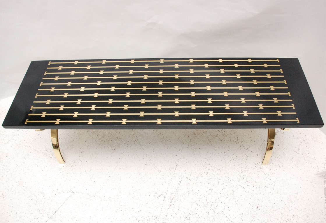 A chic polished brass and lacquered wood cocktail table. The base features two stylized figures holding the table top aloft. The ebonized and lacquered top features inlaid brass detailing. The last picture shows this table in situ in its original