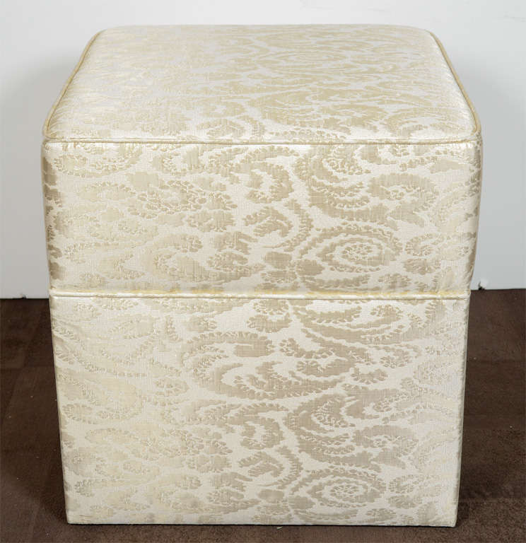 Mid-Century Hollywood Regency upholstered ottoman or vanity stool in gold silk damask print Scalamandre fabric. The ottoman has a chic cube form with tight seat design, and self welt details.  Upholstery has a crème silk background with raised gold