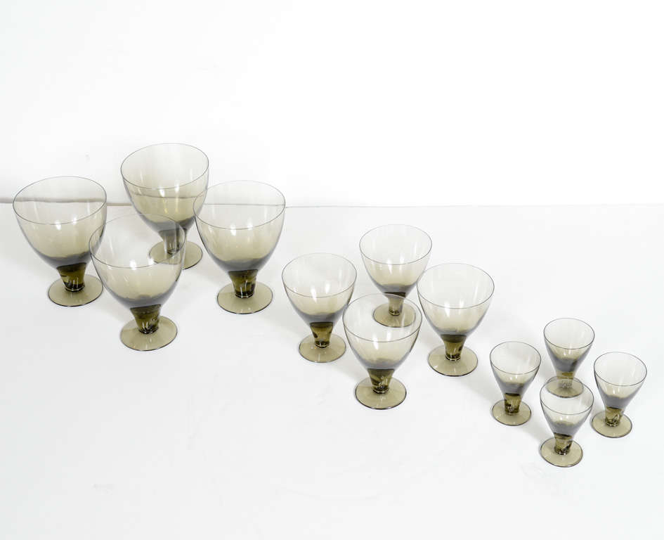 Exquisite hand blown crystal stemware set with modernist form.  The 24 piece set is a service for 8, which includes 8 water glasses, 8 wine glasses, and 8 cordial glasses. The glasses have a stylized low stem design and are comprised of  smoked grey