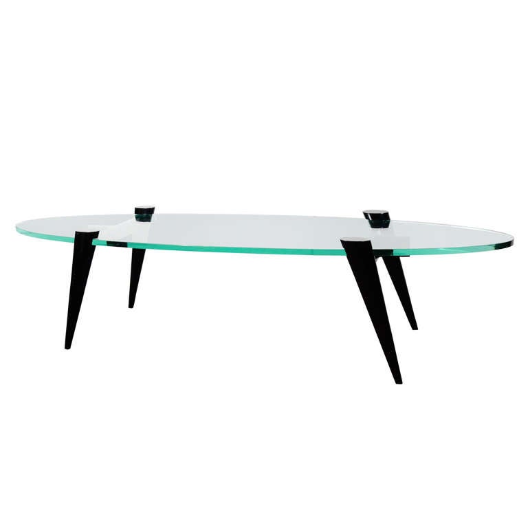 Mid-century modern cocktail table with elegant tapered leg design. Legs function as table bases in ebonized walnut wood. Fitted with thick hand bevelled elliptical or surfboard glass top. Ultra modern design great looking from all angles.