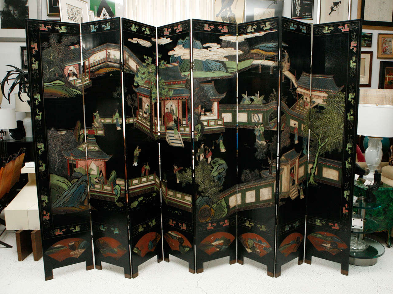 A beautiful lacquered eight-panel Coromandel folding screen with a colorful village scene on black lacquer, framed by Chinese dragons and with folding fans at the bottom of the screen. The reverse of the screen depicts a tree and flowers growing out