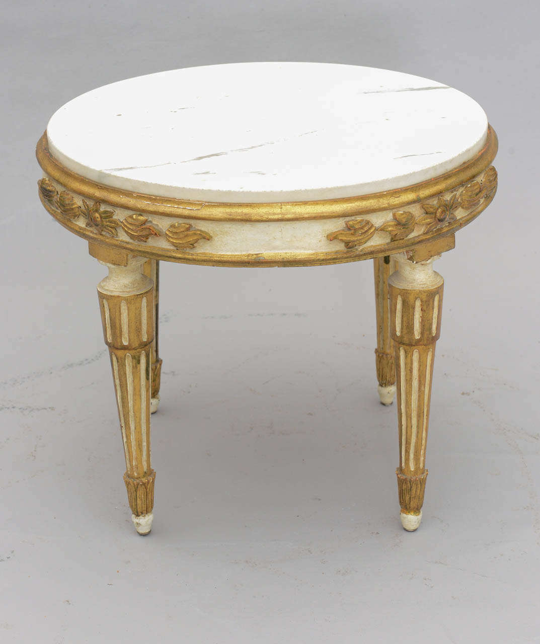 Round accent table, having white veined marble top inset in painted and parcel giltwood frame, its apron carved with foliate and laurel leaf details; raised on round fluted legs.

Stock ID: D6725