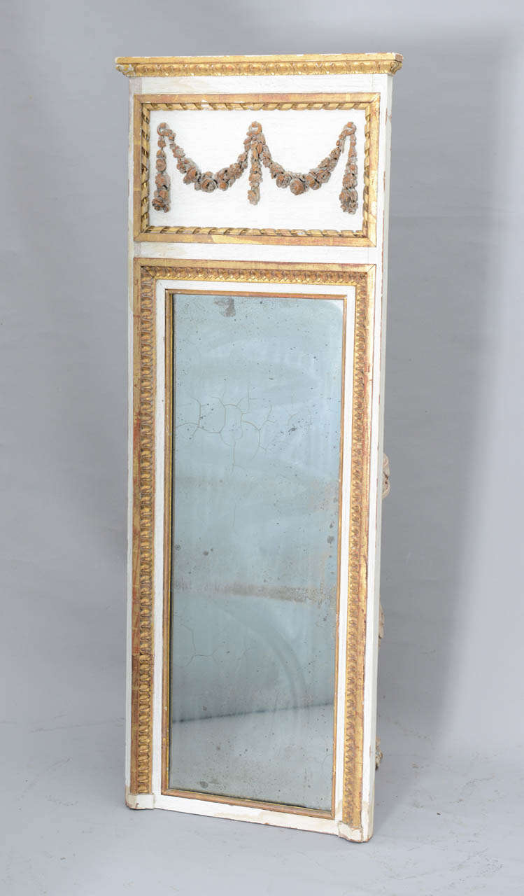 Trumeau, painted and parcel gilt with natural wear, having a gadrooned pediment with carved festooning, surmounted by molded cornice, over similarly carved border holding distressed mirror.