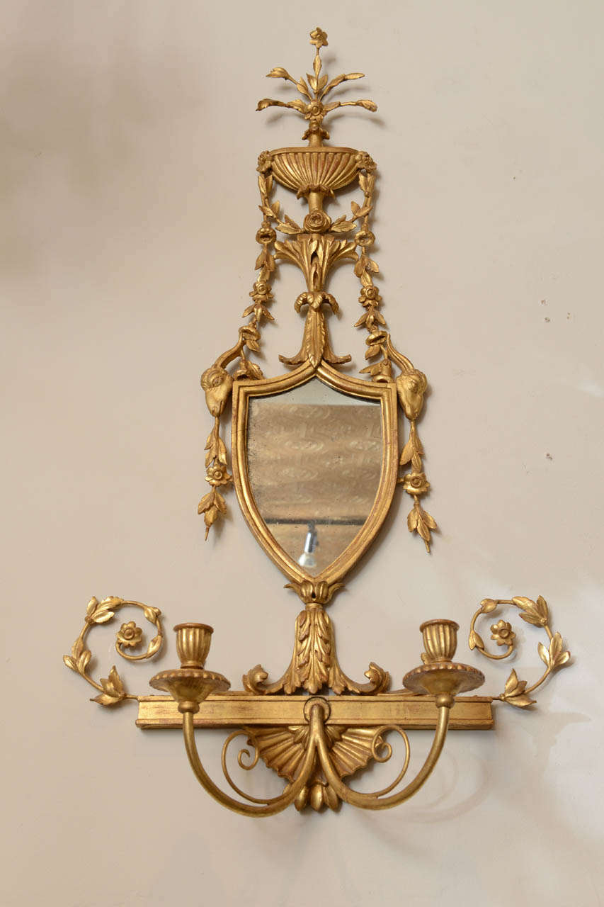 Pair of giltwood sconces, in classical form, each surmounted by carved fluted flower-filled urn draped with swags, shield shaped mirror plate, two candlearms; not electrified.

Stock ID: D6721