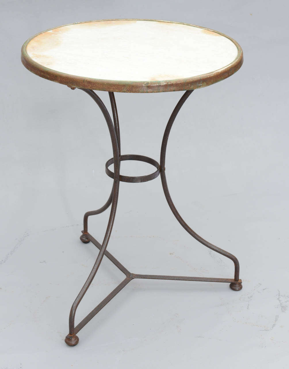 Round table, having white marble top inset in distressed iron frame, raised on three iron legs connected by stretcher.