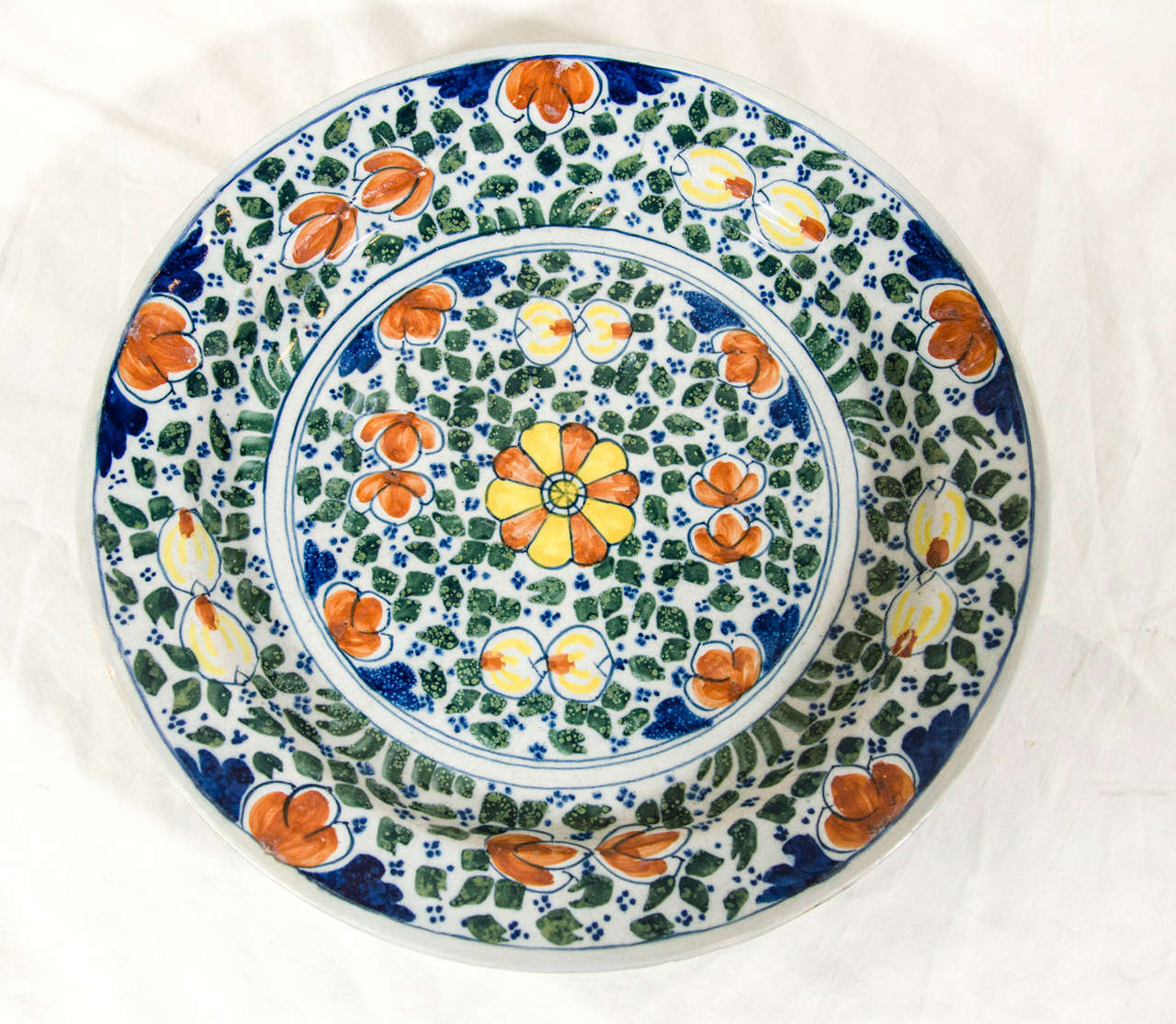 A Dutch delft charger decorated all-over with a lively design of leaves and flowers painted in green, yellow, orange and blue.