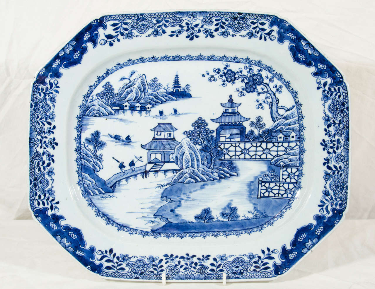 An 18th century Chinese blue and white platter showing pagodas and a waterside scene with two travelers on a bridge.