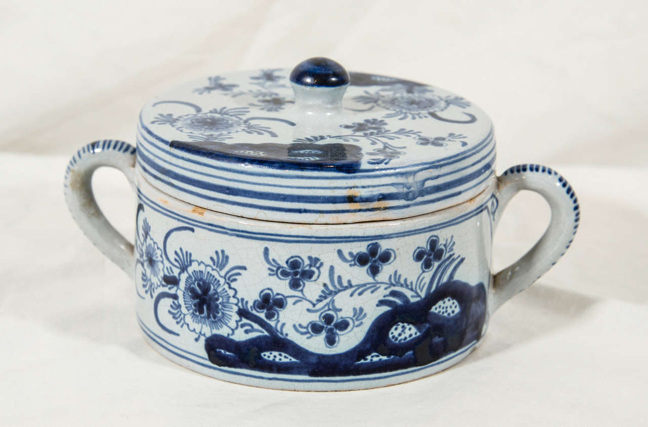 A pair of blue and white Dutch Delft covered jars each painted in cobalt showing a design of peonies and other flowers issuing from rockwork. The handles painted with stripes.