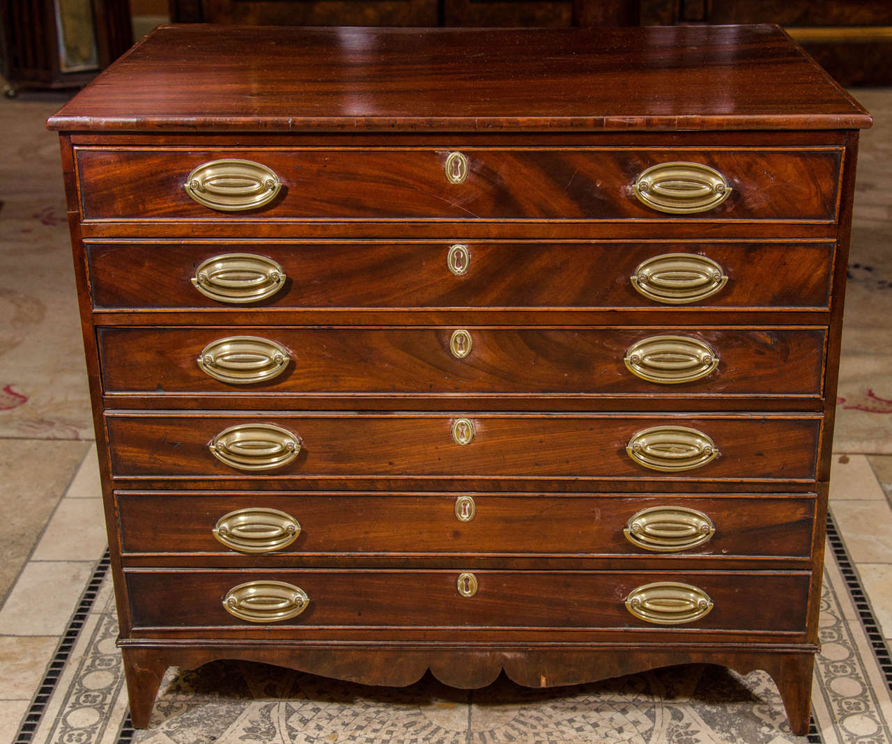 A Hepplewhite figured mahogany miniature chest of drawers or collector's cabinet, fitted with six shallow drawers and with a shaped apron and bracket feet, retaining the original oval brass hardware.