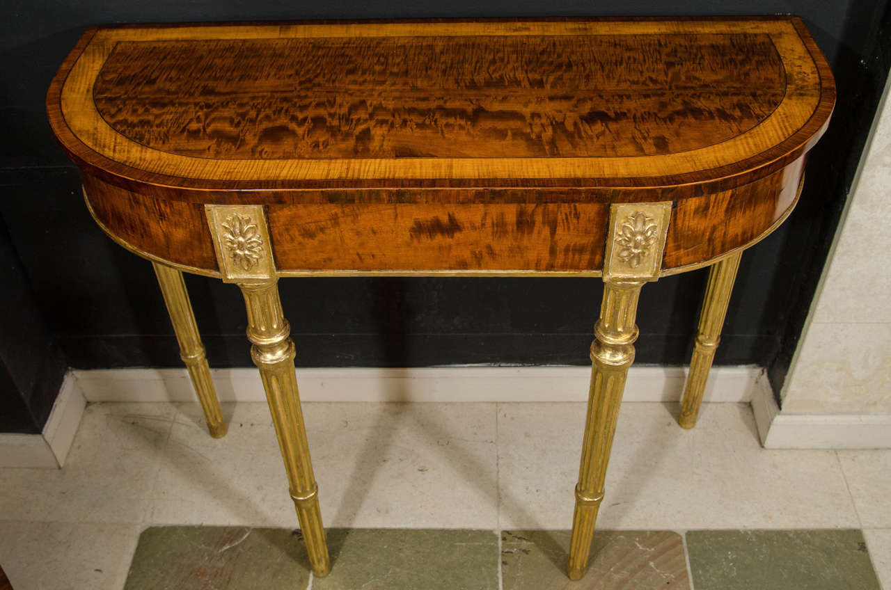 A pair of Sheraton figured mahogany and satinwood banded D-form console tables on turned and fluted gilt legs headed by paterae. Possibly American.