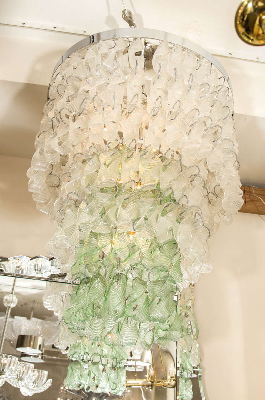 Multitiered circular chandelier composed of chains of clear and green glass ribbon form elements.