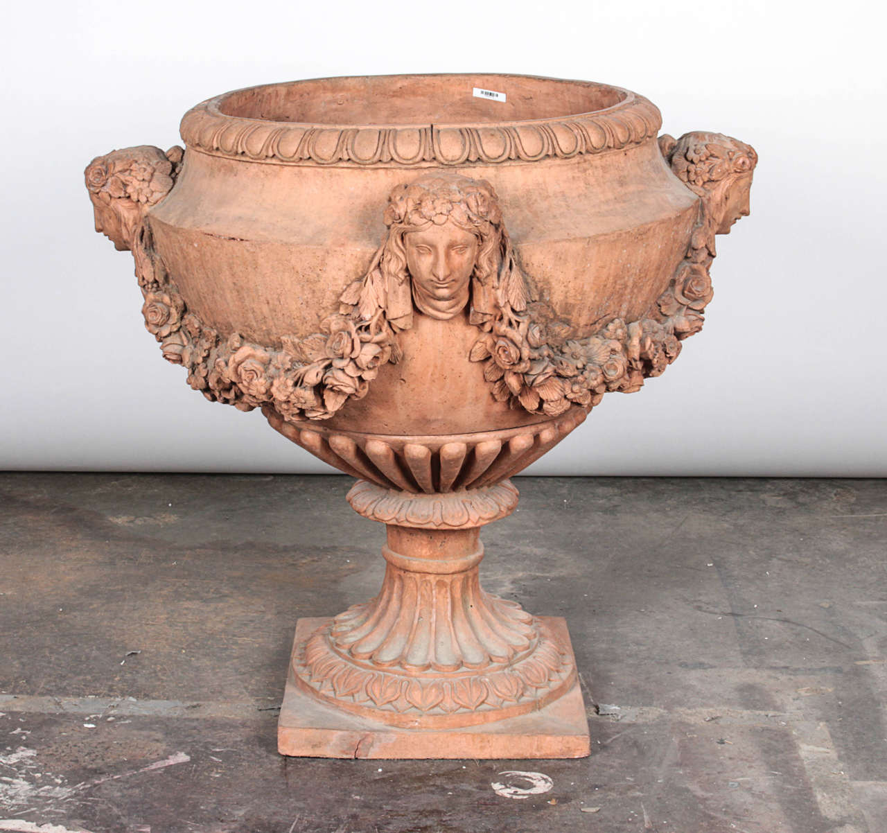 Pair of terracotta urns with the faces of a maiden on four sides. Garlands of terracotta florals connect each maiden. Each urn is consists of two pieces: a base and a bowl which rests on top.

*Not available for sale or to ship in the state of