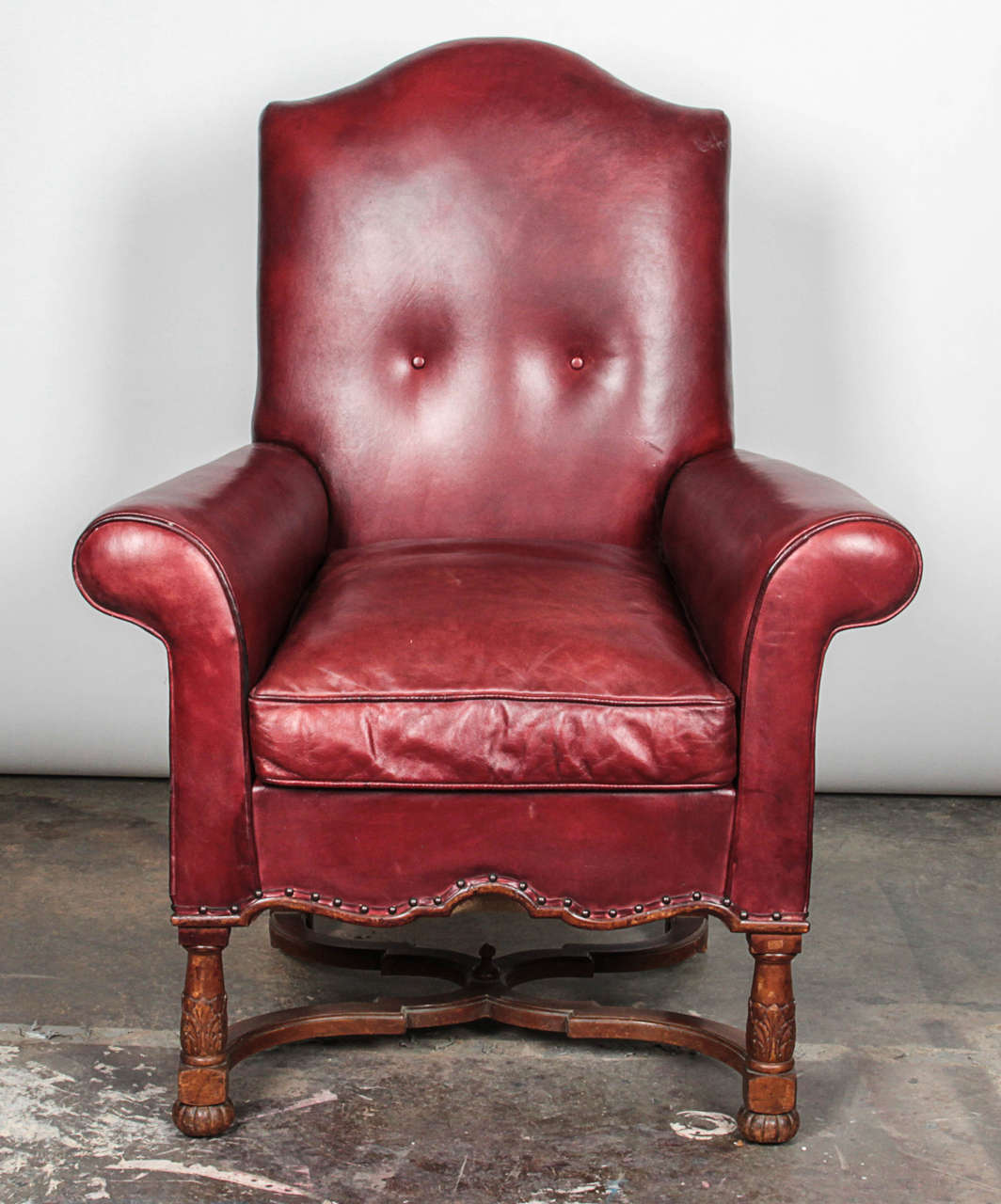 Beautiful leather chair with arched backrest, loose seat cushion flanked by out-scrolled arms, shaped rail with brass tack trim, over blocked, turned and acanthus-carved stretchered legs. Wooden finial on underside of chair is worn.

Not available