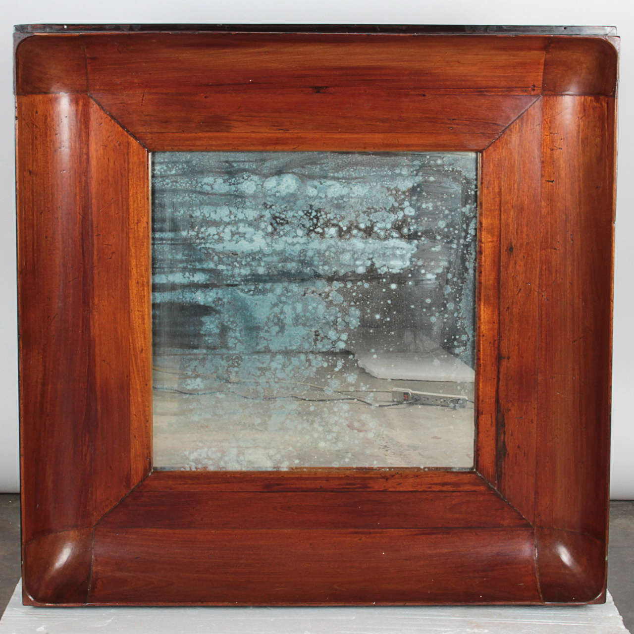 Incredibly unique antique mirror with heavy patina. Wood frame has a concave interior shape with stain that accentuates the characteristics of the wood. Outer edges of the wood have a beautiful worn black lacquer. Depth of the frame forms a ledge