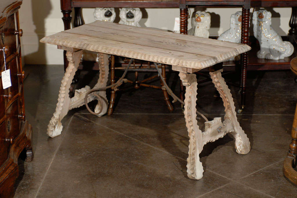 This Spanish Baroque style bleached wood coffee table from the 20th century features a rectangular top with reeded and beveled edges, over an exquisite lyre shaped leg trestle base. The splayed legs have been carved with notches on the totality of