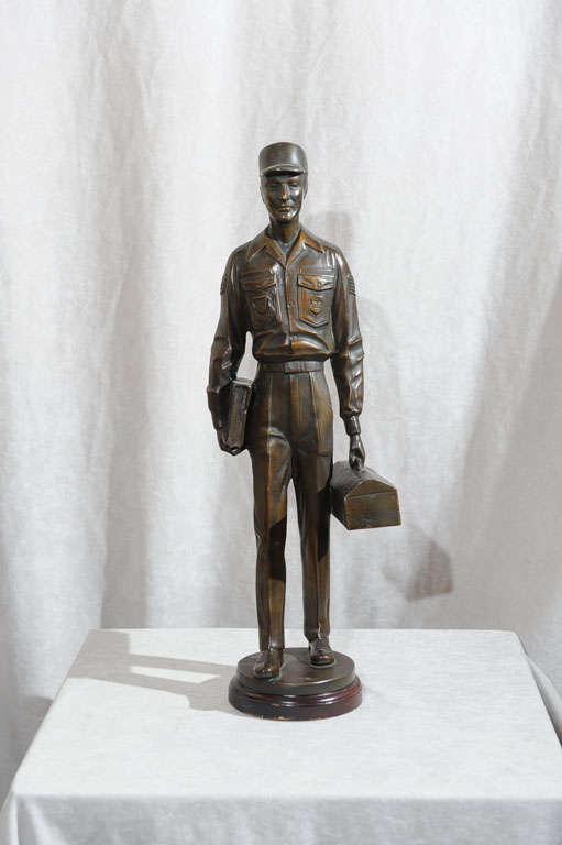 This very unusual bronze sculpture of an Air Force repair man on his way to work shows that machine age style. His square face and outfit are exemplary of this style and period. His uniform is marked 