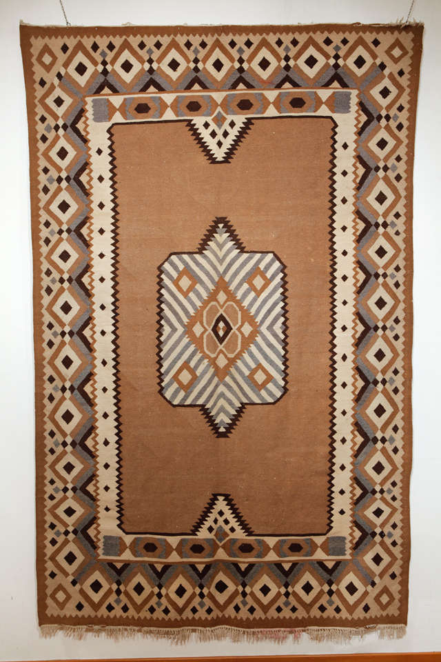 Tissé dans des tons bruns et gris, ce kilim inhabituel est décoré d'un motif géométrique influencé par l'avant-garde européenne, plutôt que d'un motif floral plus typique. Il est solidement construit avec des trames courbes caractéristiques et