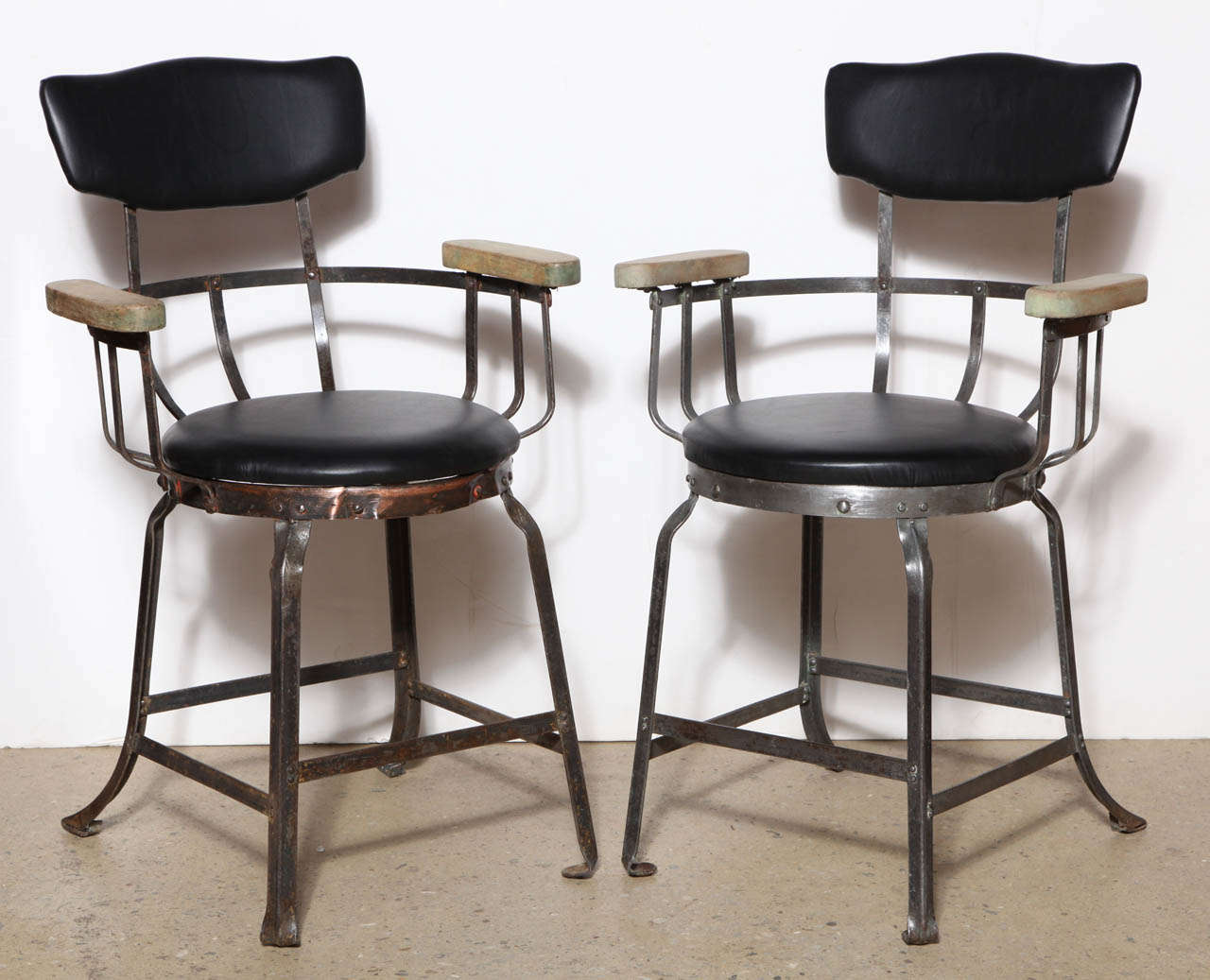 early sporting Brunswick Arm Chairs with riveted Steel construction, thick wooden Arm rests and rounded spring back. Seat and Back newly reupholstered in Black Leather.  Chairs possibly used in a Bowling Alley.  Paint removed. Great as comfortable
