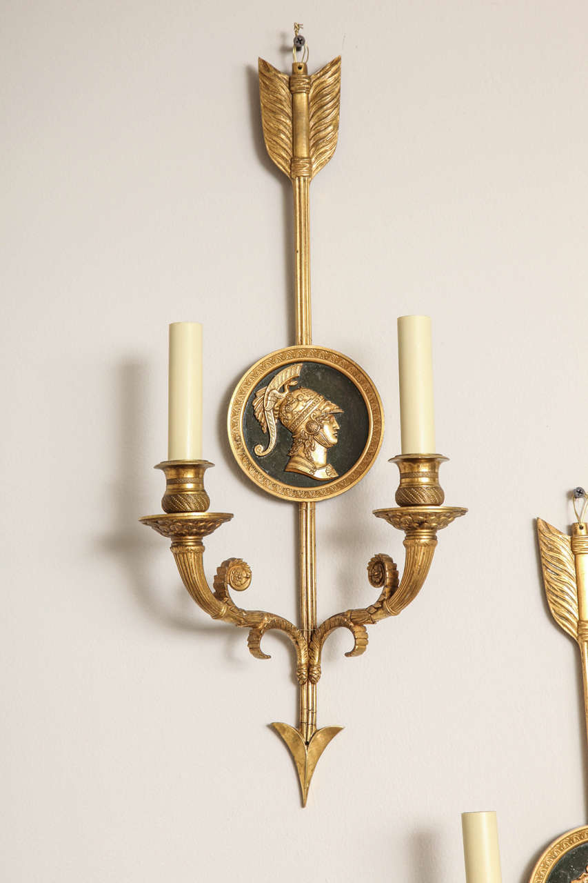 A pair of French Empire style sconces. The backplate in the form of a vertical arrow with round medallion having classical warrior in profile on a dark green ground.