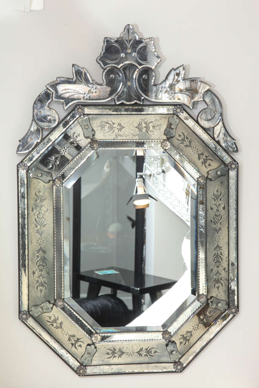A 1940s octagonal Venetian glass mirror, the clear beveled center glass surrounded by antiqued mercury silvered frame with notched edges the sections secured by glass rosettes and having leaf and floral motif carved decoration. The top surmounted by