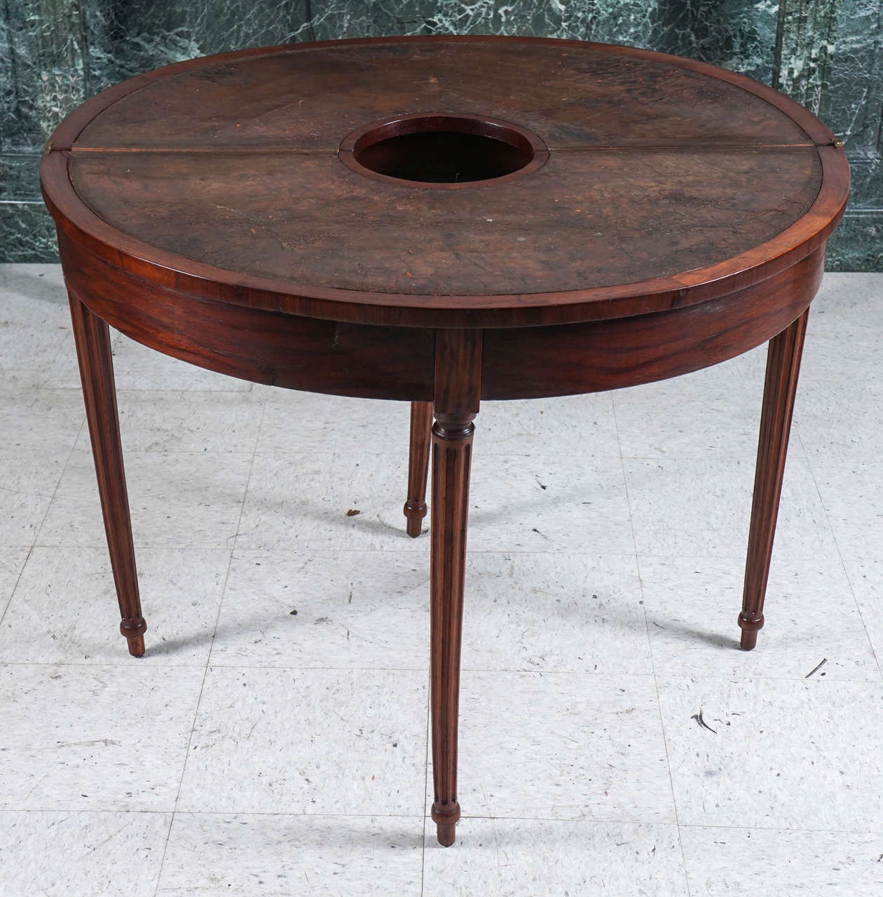 This table made in France during the brief period of the Directoire period circa 1790 is of a very unusual form. Crafted from mahogany solids and veneers the D shape opens with a slide out leg concealing a drawer and creating a round leather topped