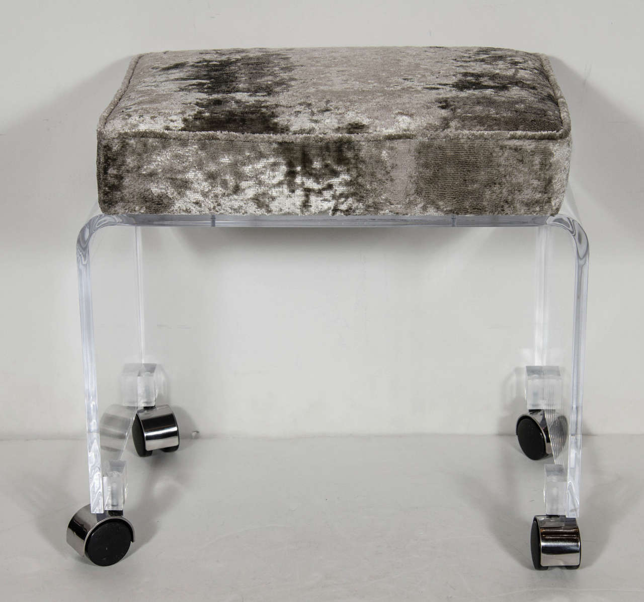 Chic Mid-Century Modernist clear Lucite bench or vanity stool in a waterfall design on chrome castors. The thick squared top cushion has been newly upholstered in a smoked pewter velvet upholstery which makes this piece a great addition to any room.