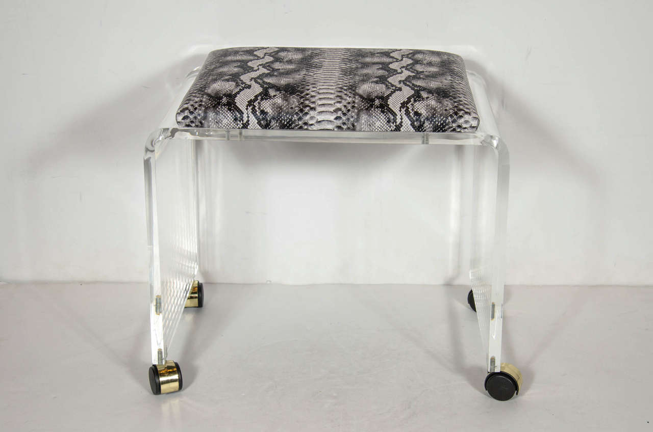 Chic Mid-Century Modernist clear Lucite bench or vanity stool in a waterfall design on chrome castors. The top cushion has been newly upholstered in a grisaille faux python fabric. Mint restored condition.

American, Circa 1970

Dimensions:
13.5