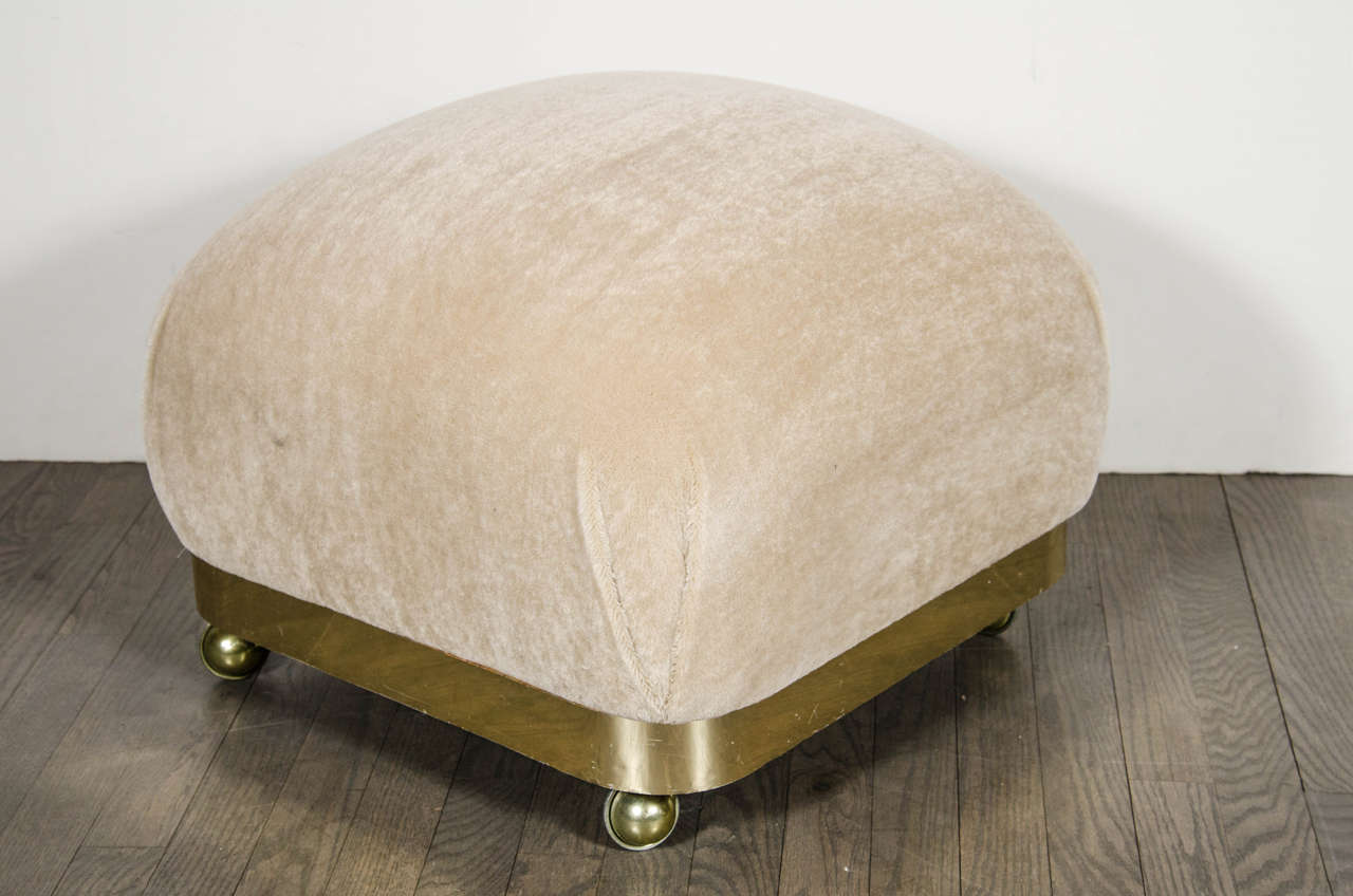Mid-Century Modernist stylized ottoman or pouf with brushed brass banding. This ultra chic ottoman or pouf features a base of brushed brass banding that has curved corners that each support spherical brass castors. The brushed brass banded base is