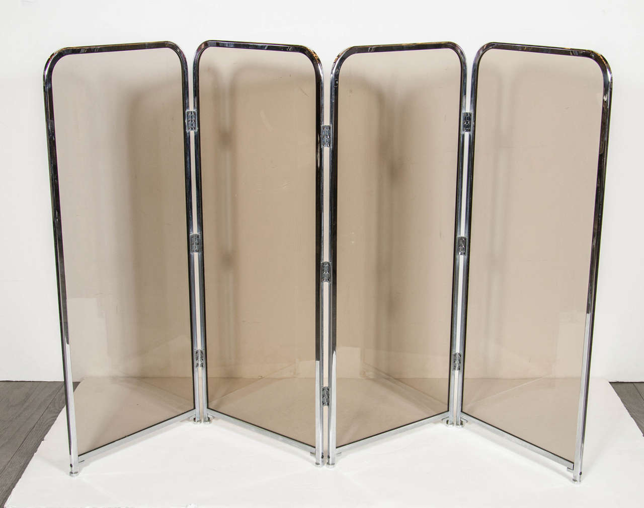 Mid-Century Modernist chrome and smoked glass fireplace screen. This chic fireplace screen features four panels total, each individually framed in polished chrome banding with curved sides on top and smoked glass inset one each panel. This fireplace