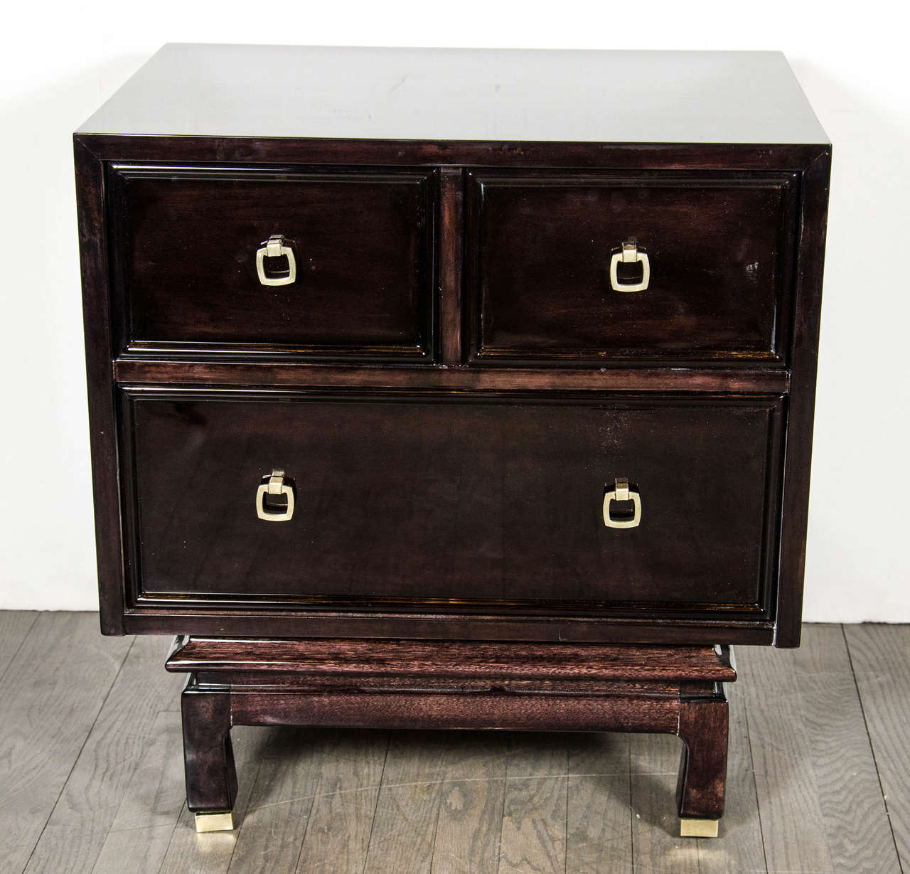 This very sophisticated pair of nightstands / end tables in ebonized mahogany features a pedestal base with brass caps on the feet. The three drawers feature stylized brass drawer pulls and are spacious for maximum storage. These pieces have been