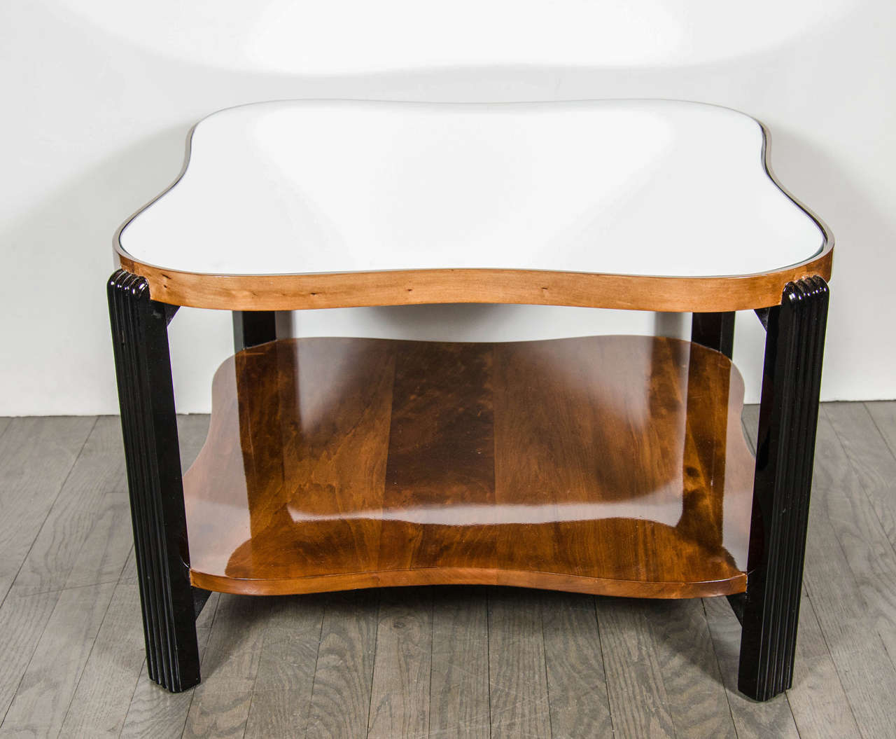 Art Deco Machine Age two-tiered cocktail table with reeded leg design and inset mirrored top.  This cocktail table features a bottom tier in book-matched Walnut and the top tier having an inset mirrored top while being framed in book-matched Walnut