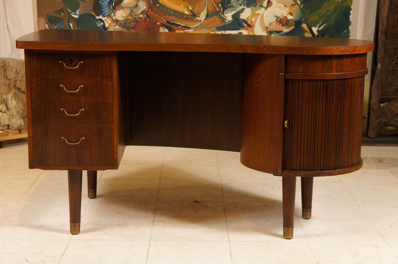 Curved mahogany desk attributed to Danish designer Kai Kristiansen, mid-century modern, with swivel drawer and bar feature at one end and 4 drawers with brass pulls at the other.  The back side is configured with shelves for books and storage.  