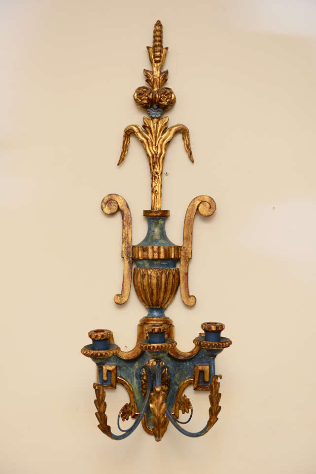 Pair of wall sconces, painted and parcel gilt, each shield-shaped backplate surmounted by carved fluted urn with exaggerated scrolling handles, holding flourish of rosettes, and wheat, a trio of C-scroll foliate candlearms terminate in like-carved