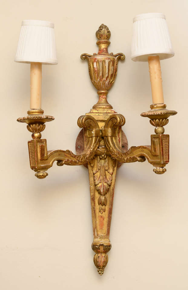 Pair of sconces of carved giltwood, each having two scrolling candlearms, a backplate surmounted by a fluted urn.  Electrified.

Stock ID: D6579