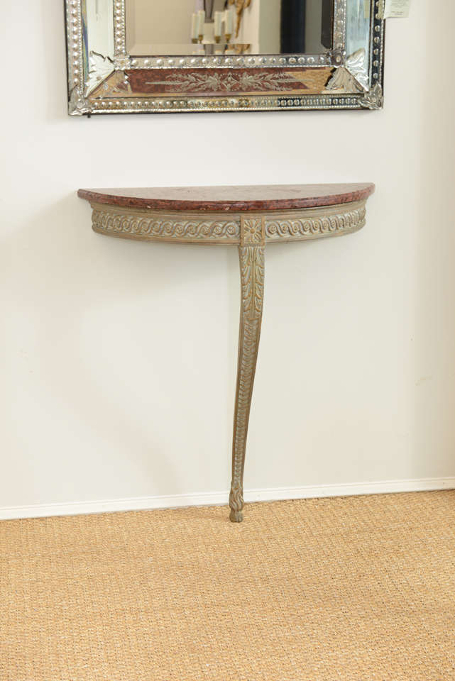 Wall mounting demilune table, having distressed painted finish, marble top on apron of carved wood with vitruvian scroll design centered with rosette, atop single leg carved with acanthus and laurel leaf motifs, raised on paw foot.