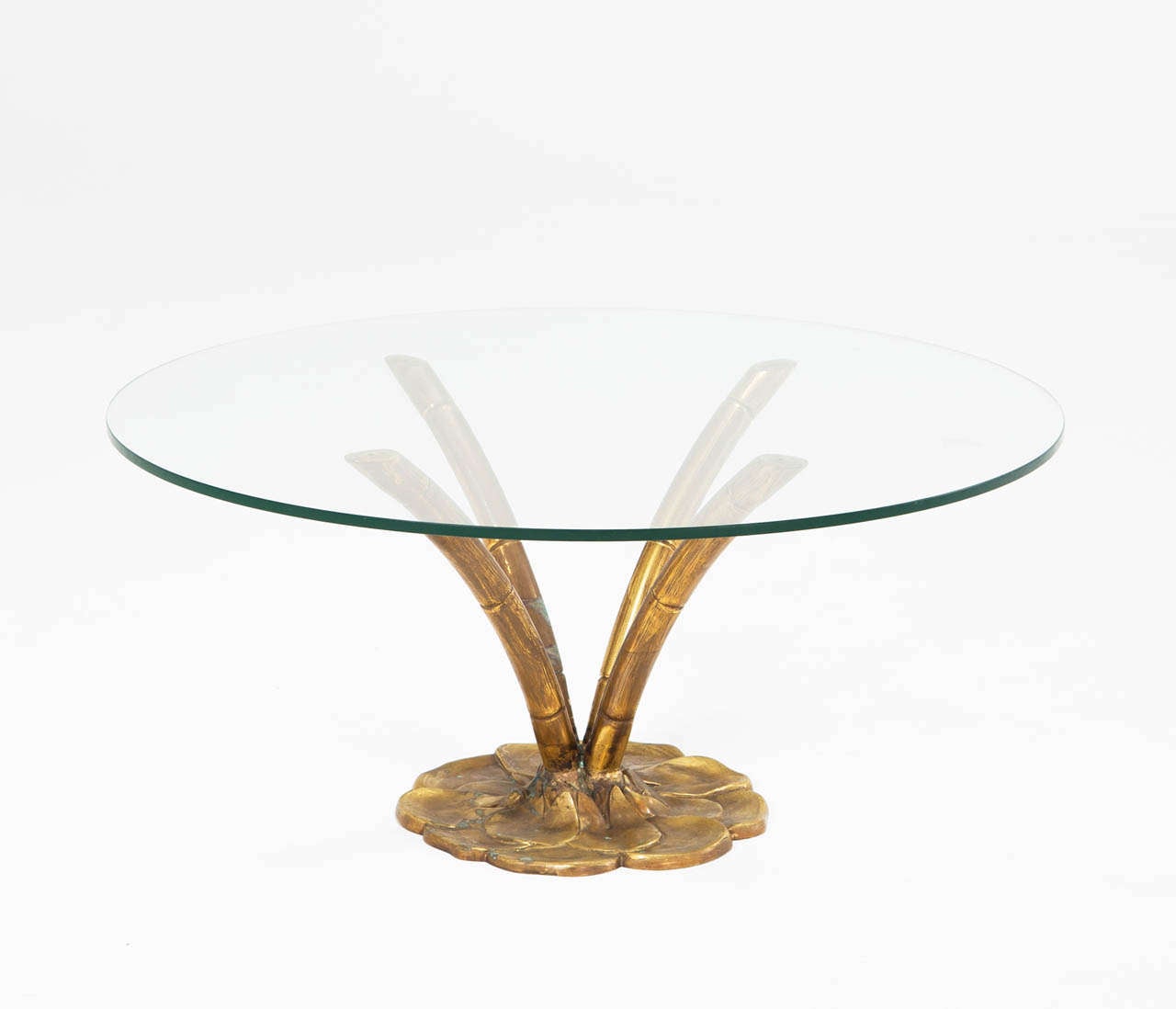 Interesting Faux bamboo coffee/side table with round glass top.

Base created as a pedestal ending in 4 separate bamboo sterns, with nice patina to the brass. Clear glass, round table top to accentuate the brass base. 
