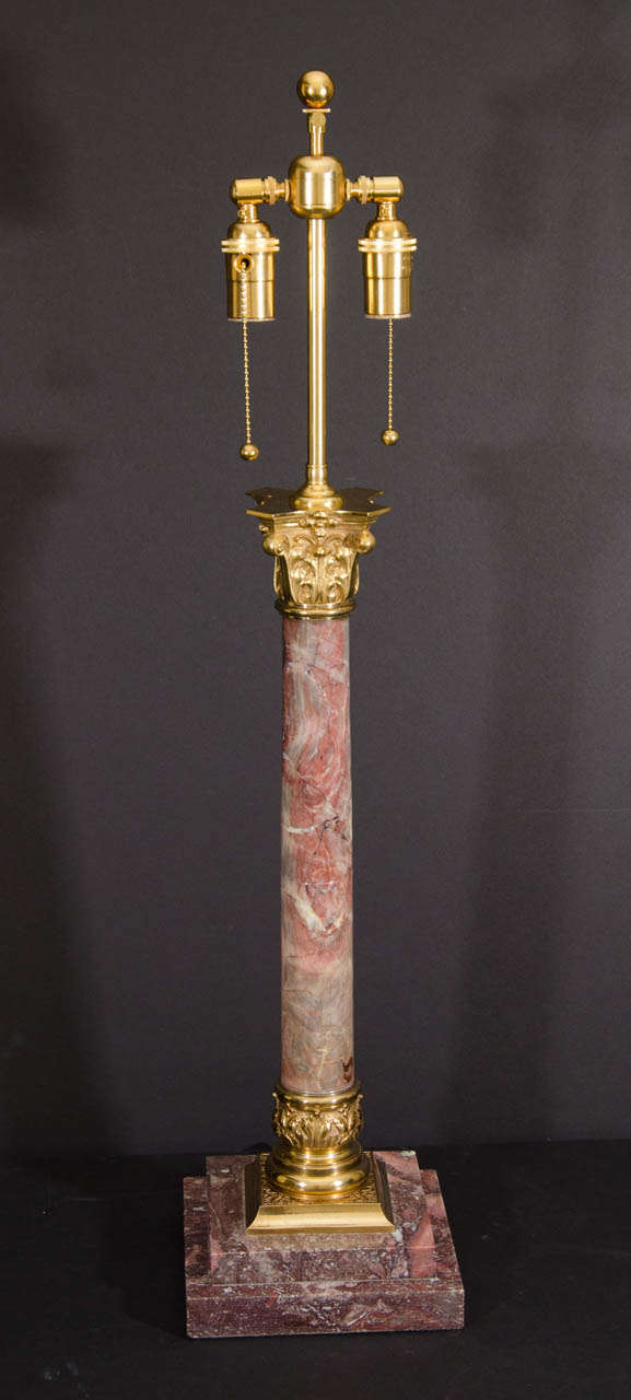 Rouge colored marble and gilt bronze two light table lamp made in the Neoclassical style with corinthian capital and stepped base.