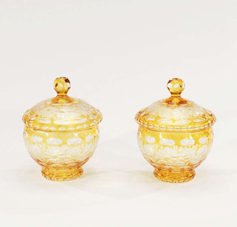 Both useful and decorative, this lovely pair of crystal covered jars provide a beautiful golden amber focal point. The amber casing is cut to clear with an all-over floral motif and the foot and finial are also cut. Perfect for a mantel, filled with