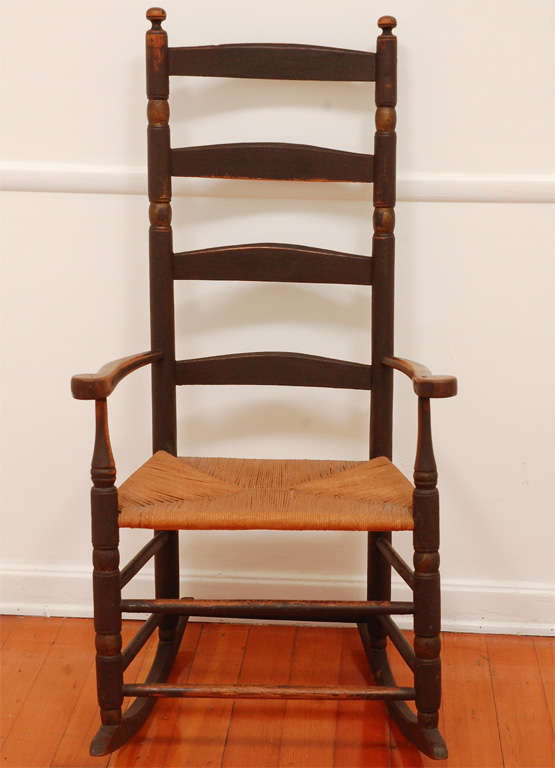 Fantastic form and original brown paint with gilded turnings.This 19thc ladder back rocker has a old replace rush seat.The rocker is very sturdy and comfortable .The patina is the best.This is from a private collection in New England.