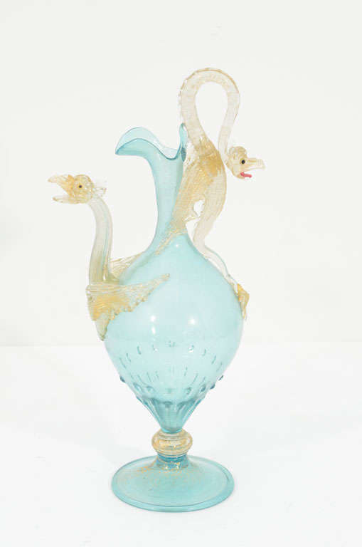 The body and foot of this ewer are executed in pale-turquoise glass. The elaborate handle and spout are modeled as clear glass winged dragons with a pink tongues and yellow and black cane eyes. The body of the ewer is executed in the