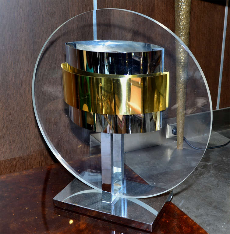 The lamp has a large round Lucite panel with chrome and brass details on each side. This is an oversized table lamp with simple lines to make a grand statement.