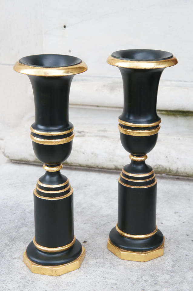 This dramatic and decorative pair of urns made in France in the 1920's are in the popular empire revival style. Turned as a rather stretched Campania urn on a stand the vases are then finely water gilded at the edges of each turned element. The